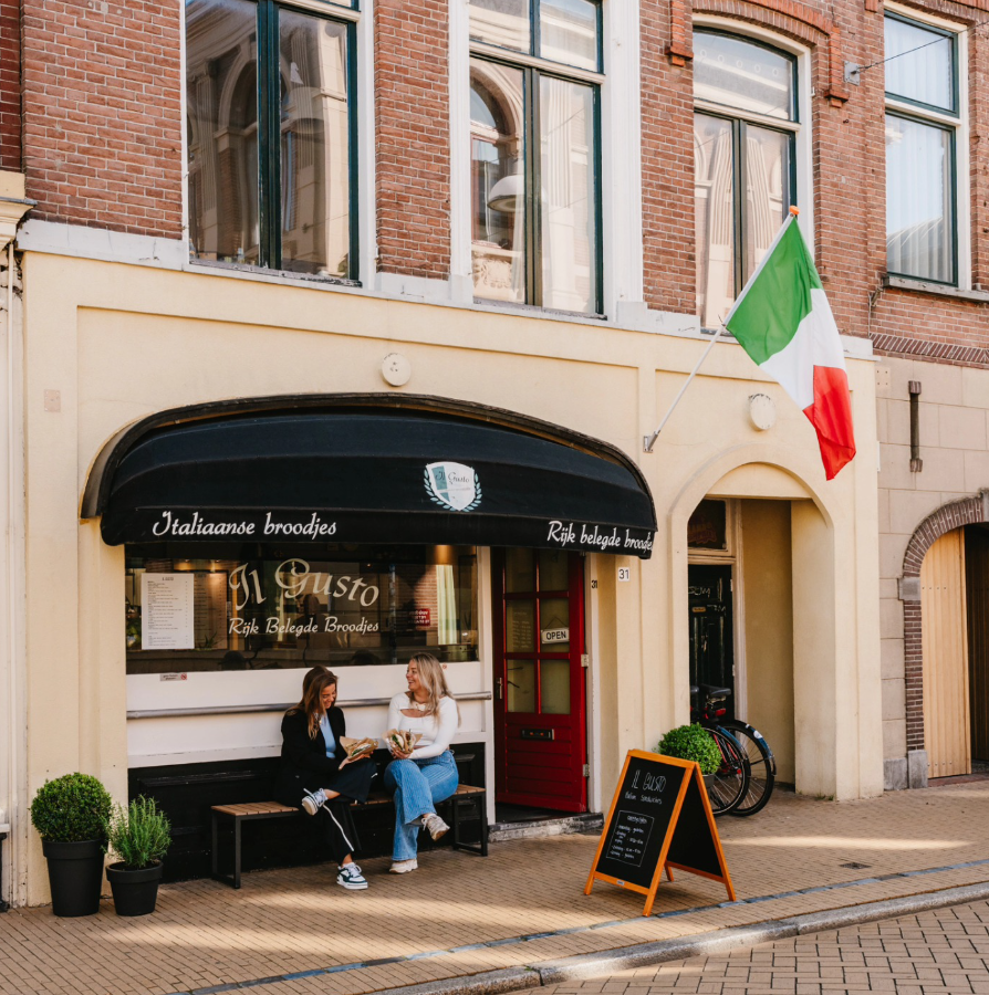 De crèmekleurige gevel van Il Gusto met donkere luifel en rode deur